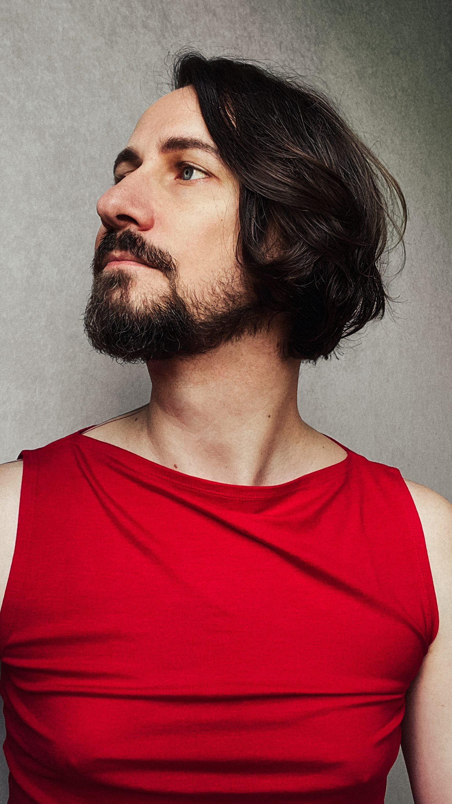 Portrait of René Gebhardt, freelance art director and designer in Berlin, wearing a red sleeveless shirt, looking to the side, with a neutral background.